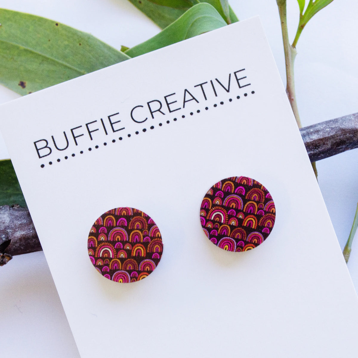 Round Purple Pattern Stud Earrings on Buffie Creative card packaging, featuring a vibrant arch and circle Indigenous pattern in deep purple, pink, orange, and yellow, designed by Buffie Punch.